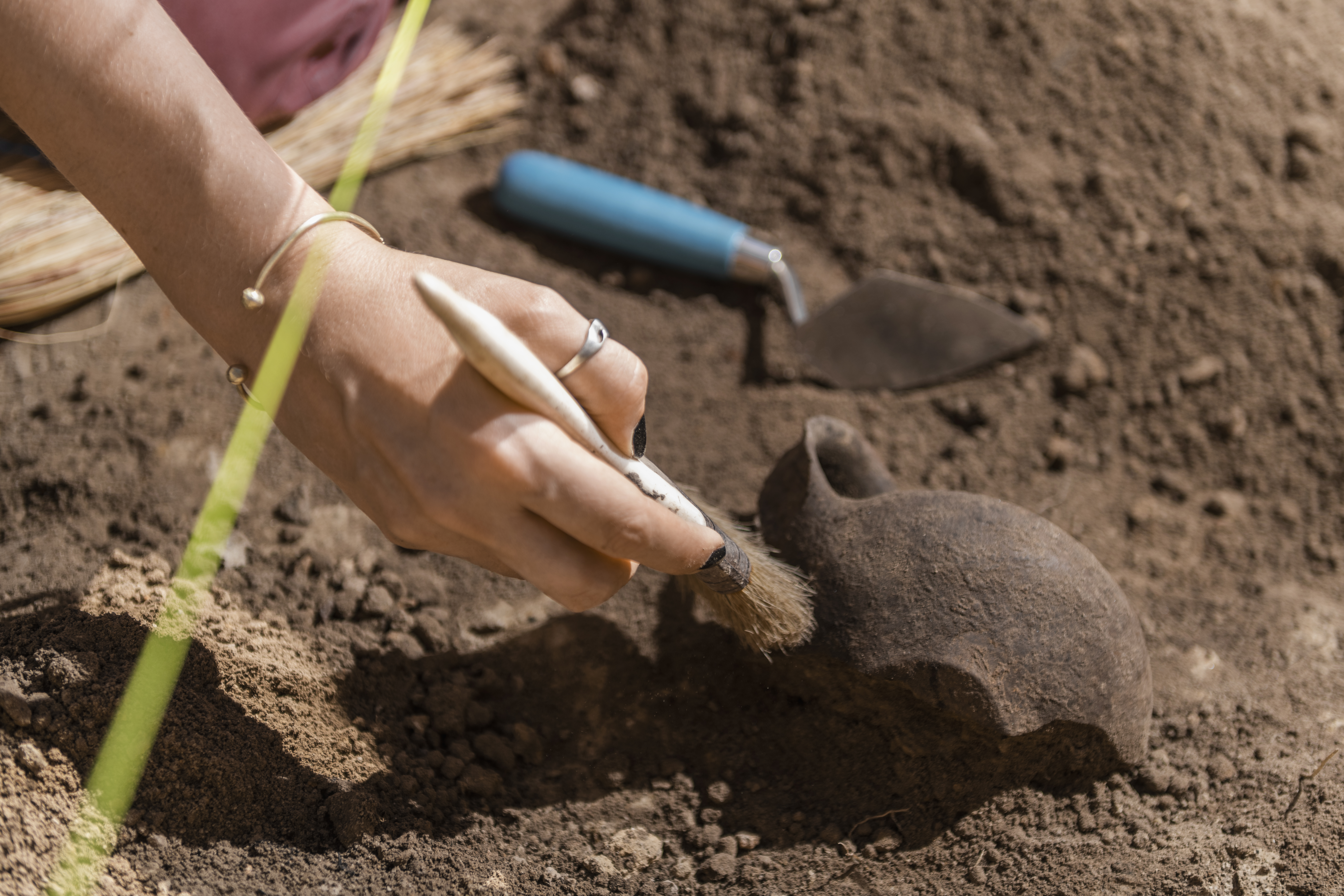 Female archaeologist digging up ancient pottery object at an archaeological site.